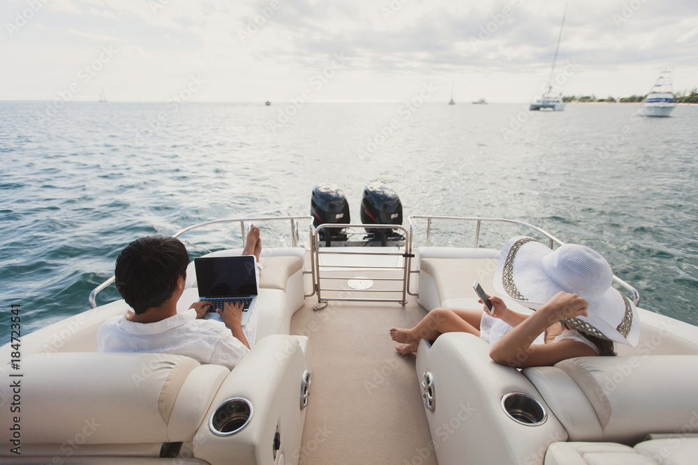 Handsome man and woman on deck of yacht with mobile phone and laptop