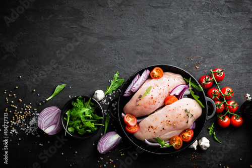 Fresh raw chicken meat, fillet marinated with spices, onion and tomatoes on black background. Top view photo