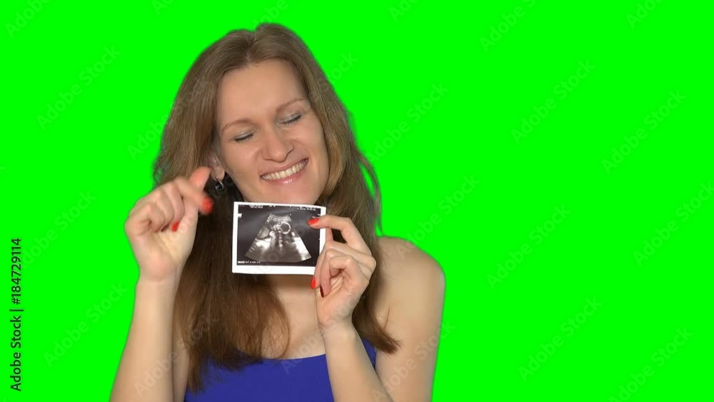 pregnant woman girl is holding sonogram of tummy, looking at camera and smiling.