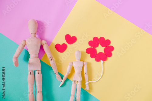 Wooden man figure holding red heart balloon. Wooden human dummy on pink, blue and yellow background with copy space for your text. Concept for valentine's day celebration or couple of love. photo