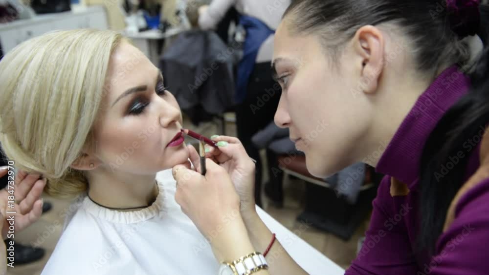 One visagiste makes hairstyle and other paints lips to girl model. Beauty salon - woman doing hair styling and makeup One visagiste makes hairstyle and other paints lips to girl model. Beauty salon - woman doing hair styling and makeup