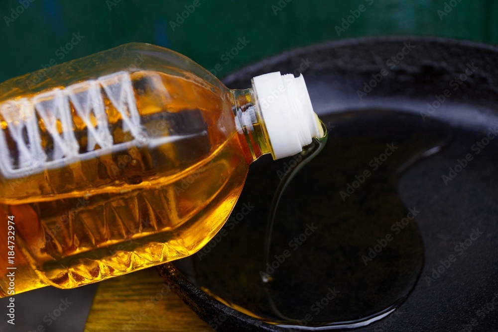 жёлтое подсолнечное масло наливается с бутылки на чёрную сковороду