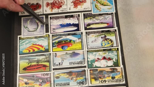 Collector philatelist leafs through the album with a collection of postage stamps, takes out the stamp from a cell by tweezers, looks at it through a magnifying glass 