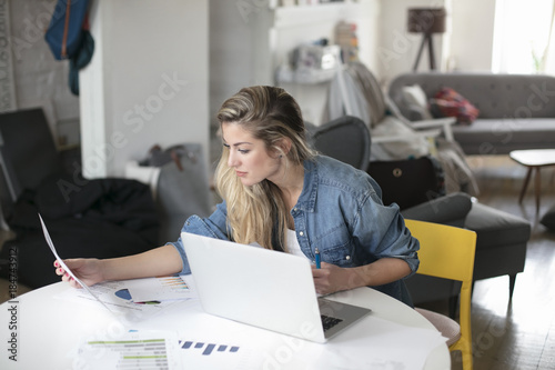 Young beautiful woman works for a computer from a home with a laptop on a white desk as a freelancer