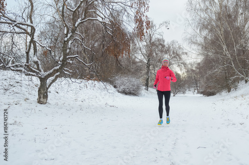 Winter running in park: happy active woman runner jogging in snow, outdoor sport and fitness concept 