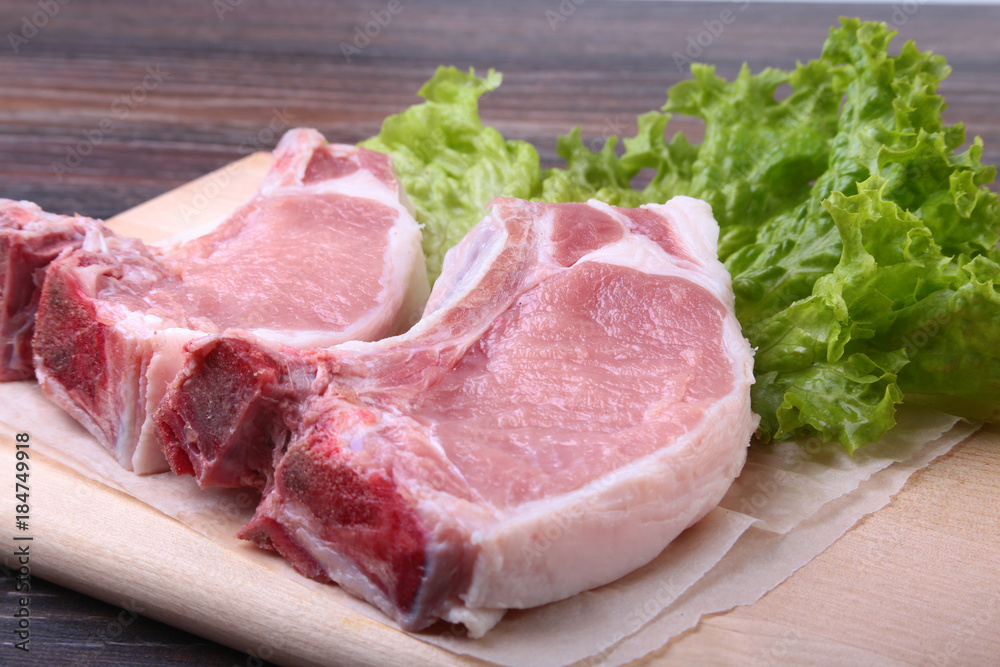 Raw pork steak with spices Leaves lettuce on wooden cutting board. Ready for cooking. Raw pork steak with spices Leaves lettuce on wooden cutting board. Ready for cooking.