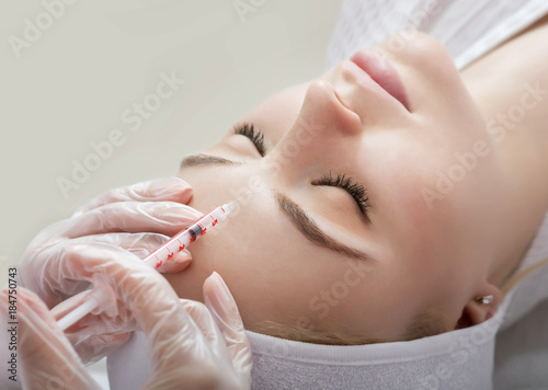 Young woman gets beauty facial injections in salon.