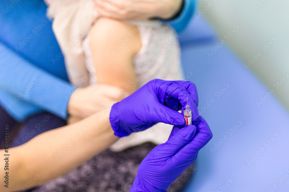 Doctors hand in ultraviolet gloves holding syringe before kids vaccination against flue Doctors hand in ultraviolet gloves holding syringe before kids vaccination against flue