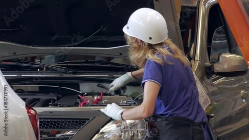 worker woman is tightening caps of capacities for technical liquids inside a car on a car factory