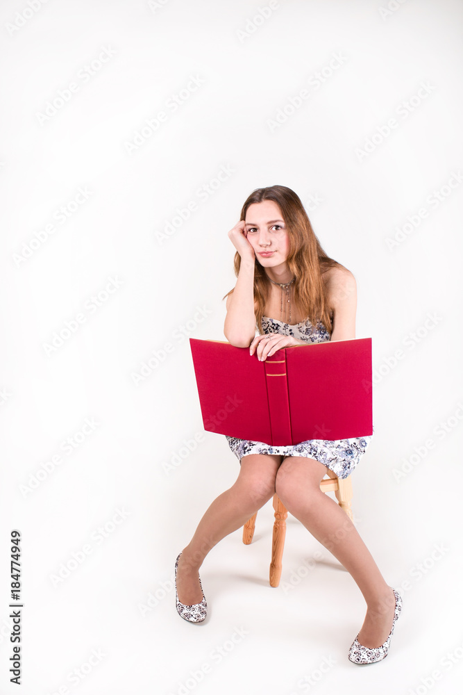 Bored pretty girl sitting on a stool with a big red book Bored pretty girl sitting on a stool with a big red book