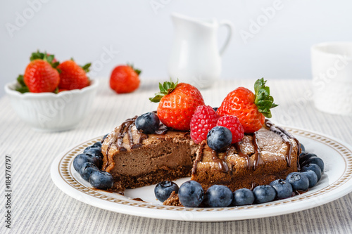 Big chocolate cheesecake with blueberry strawberry raspberry on a round plate.