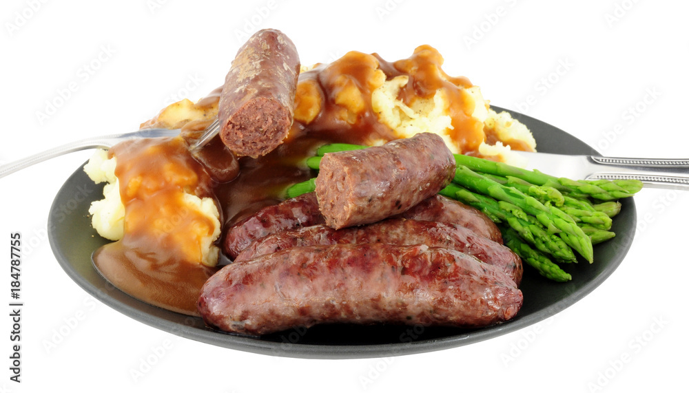 Fried venison sausages meal with mashed potatoes and asparagus on a black plate isolated on a white background