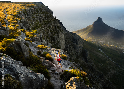 Trail runner running along a trail on the top of Table Mountain in Cape Town while out training in the mountains at sunset