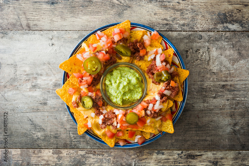 Mexican nachos with beef, guacamole, cheese sauce, peppers, tomato and onion in plate on wooden table. Top view photo