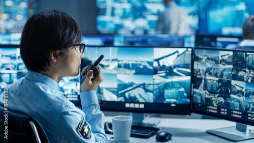 In the Security Control Room Officer Monitors Multiple Screens for Suspicious Activities, He Reports any Unauthorised Activities in His Walkie-Talkie. He's Surrounded by Monitors. photo
