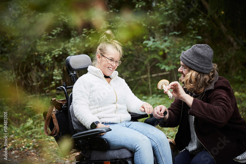 Male caretaker showing mushroom to disabled woman in wheelchair at forest photo