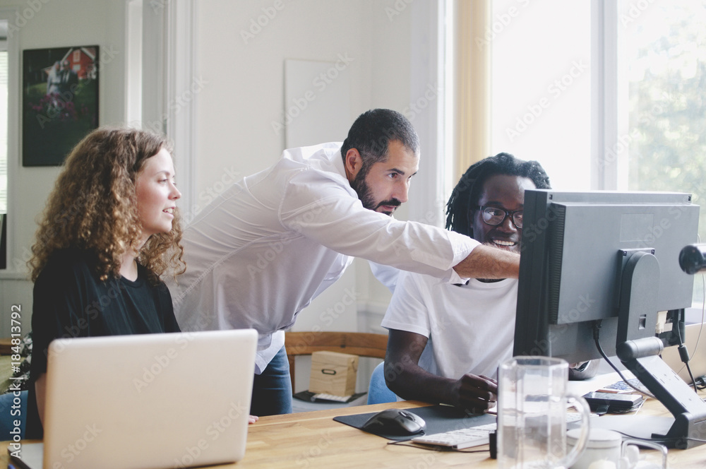 Multi-ethnic business people discussing over computer at table in creative office Multi-ethnic business people discussing over computer at table in creative office