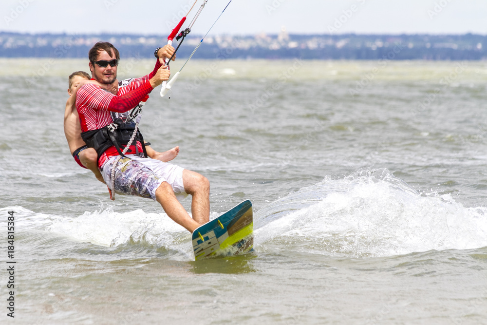 Fototapeta premium Dad and son are kitesurfing on the sea. The son clings to Papa's back