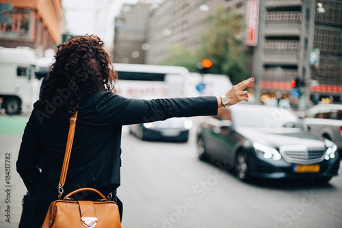Rear view of mid adult businesswoman hailing taxi on street in city photo