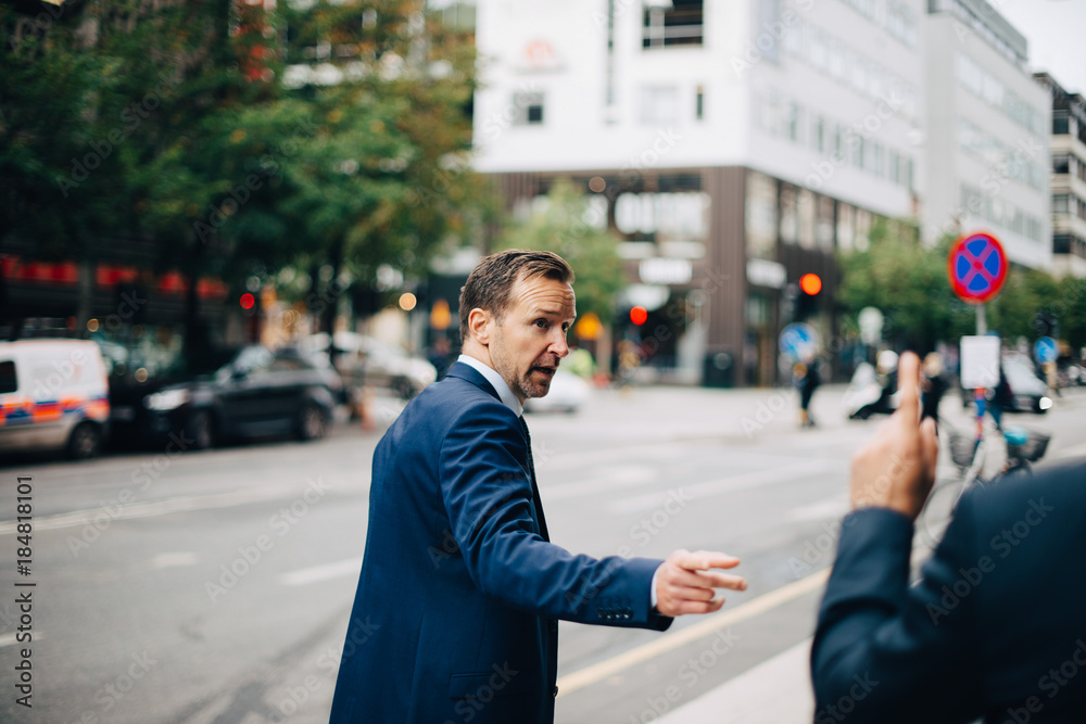 Rear view of businessman gesturing to male colleague on sidewalk in city Rear view of businessman gesturing to male colleague on sidewalk in city