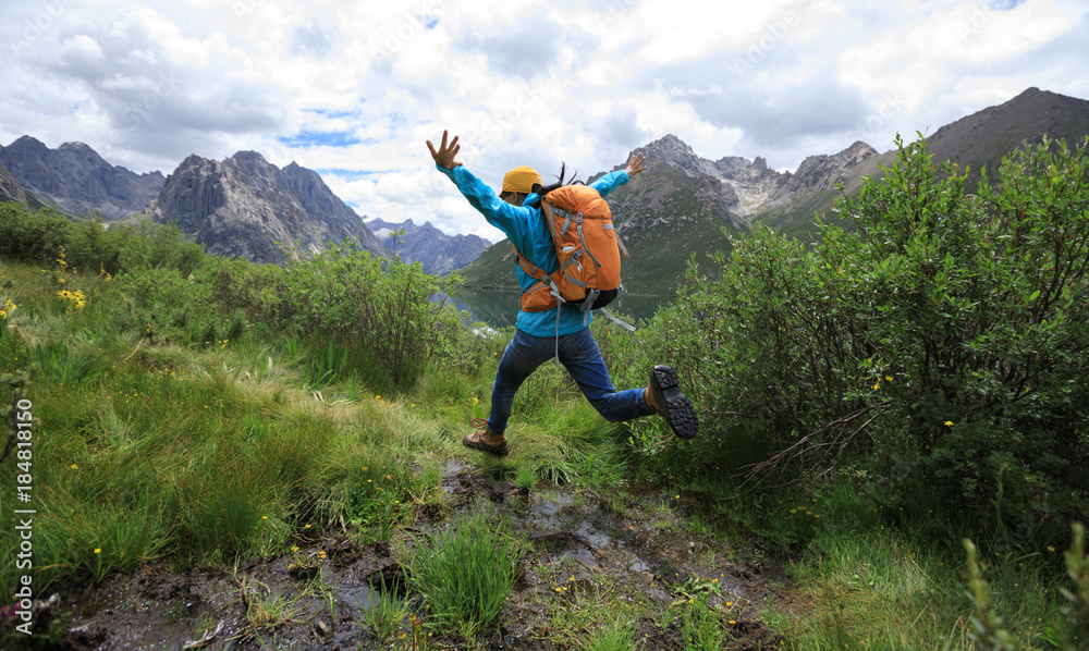 young backpacking woman jumping over water in mountains