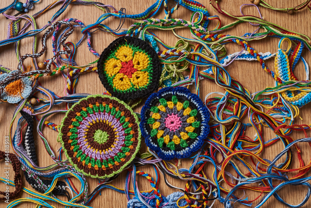Different kind of knitted colorful bracelets and earrings are chaotically lying on the table. In the lower left side there are three big knitted drink coasters.