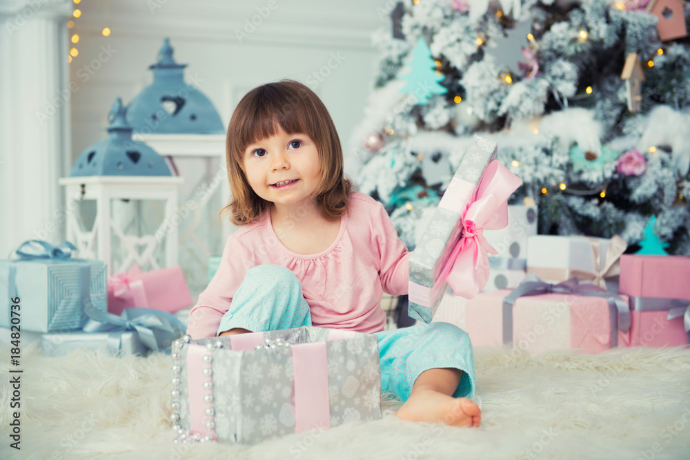 Little baby girl opens New Year gift near Christmas tree