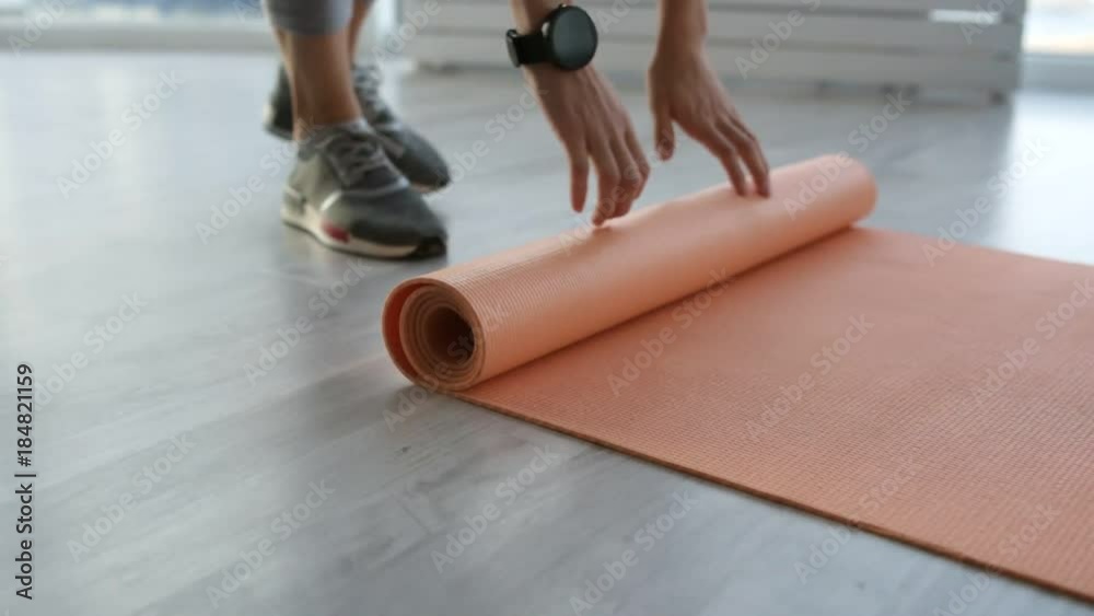 Preparation. Close up of energetic woman slowly unrolling training mat on the floor