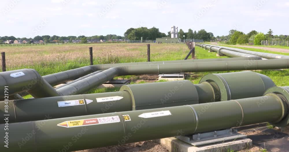 Field pipelines for oil, steam, gas transport in rural area. High-efficiency pumps and Schoonebeek skyline in background. SCHOONEBEEK,THE NETHERLANDS - JULY 2016 Field pipelines for oil, steam, gas transport in rural area. High-efficiency pumps and Schoonebeek skyline in background. SCHOONEBEEK,THE NETHERLANDS - JULY 2016