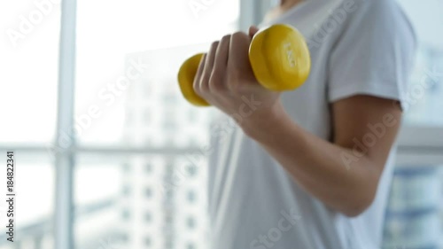 Strong and healthy. Close up of young sportive woman standing in front of you while training with light weights