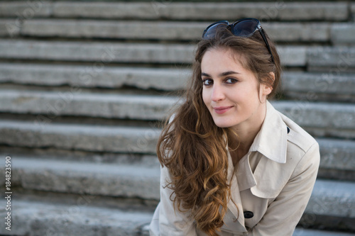 Young beautiful woman wearing beige jacket and sunglasses over stairs