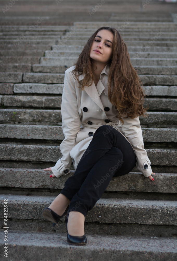 Young beautiful woman wearing beige jacket sitting on concrete stairway Young beautiful woman wearing beige jacket sitting on concrete stairway