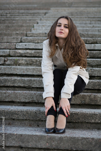 Young beautiful woman wearing beige jacket sitting on concrete stairway © Yevgeniy Zateychuk