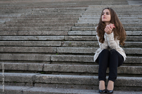 Young beautiful woman wearing beige jacket sitting on concrete s