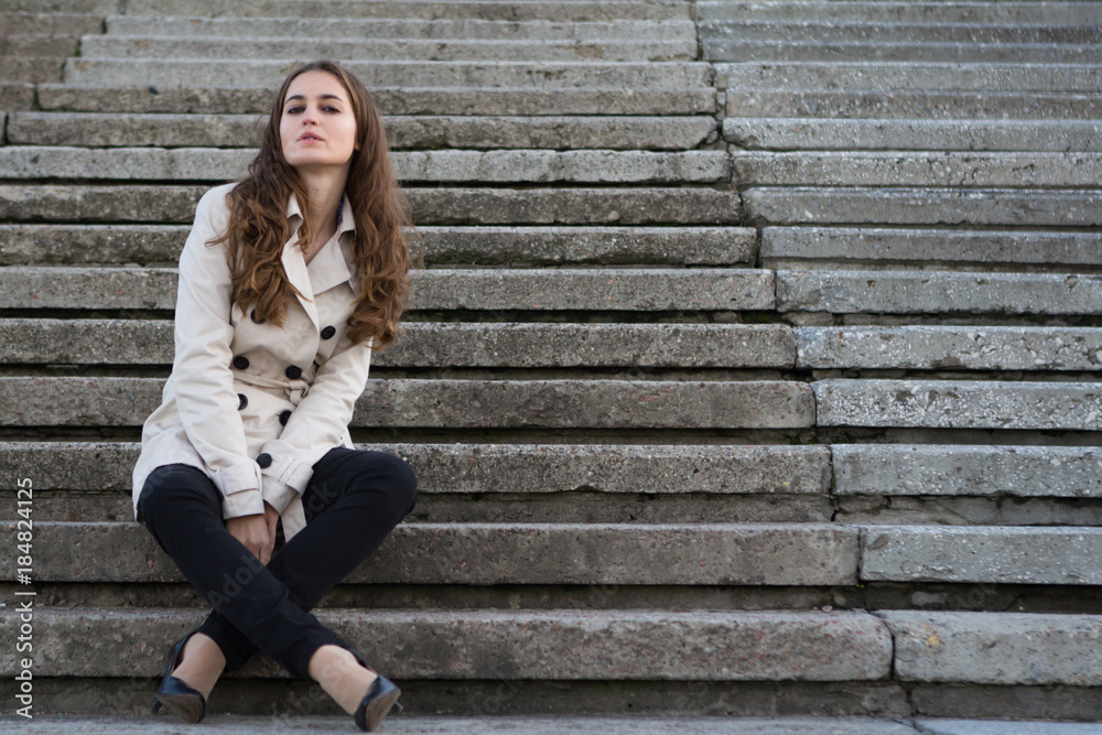 Young beautiful woman wearing beige jacket sitting on concrete stairs Young beautiful woman wearing beige jacket sitting on concrete stairs