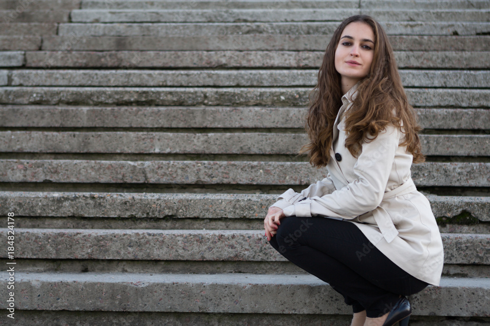 Young beautiful woman wearing beige jacket sitting on concrete stairs Young beautiful woman wearing beige jacket sitting on concrete stairs