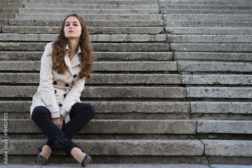 Young beautiful woman wearing beige jacket sitting on concrete stairs © Yevgeniy Zateychuk