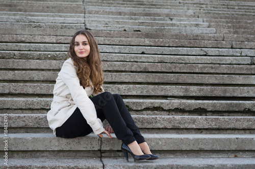 Young beautiful woman wearing beige jacket sitting on concrete stairs