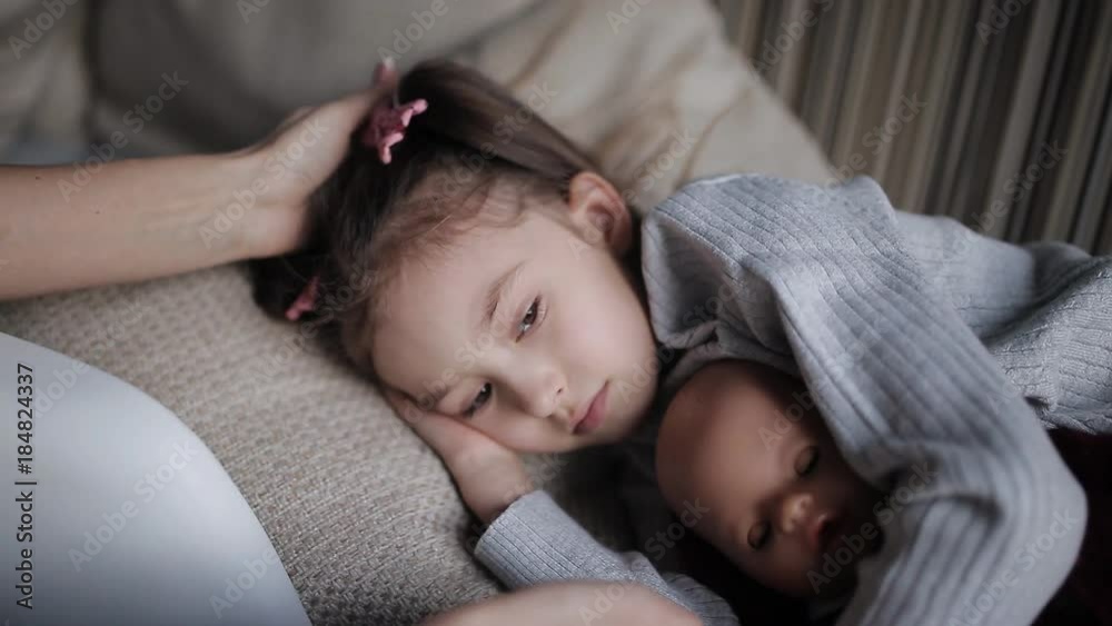 beautiful little girl on a sofa falls asleep and hugging a doll. Mom strokes a sleepy daughter beautiful little girl on a sofa falls asleep and hugging a doll. Mom strokes a sleepy daughter