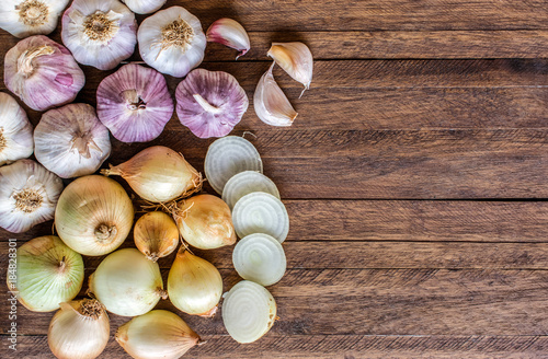 Onions and cut onions, purple whole garlic and garlic cloves on top of a light wooden background, with lots of texture and copy space