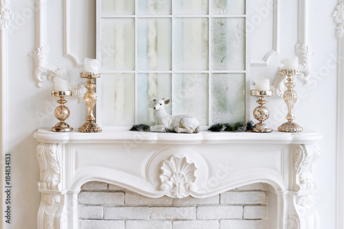White mantelpiece with candles and christmas decorations. Classic interior.