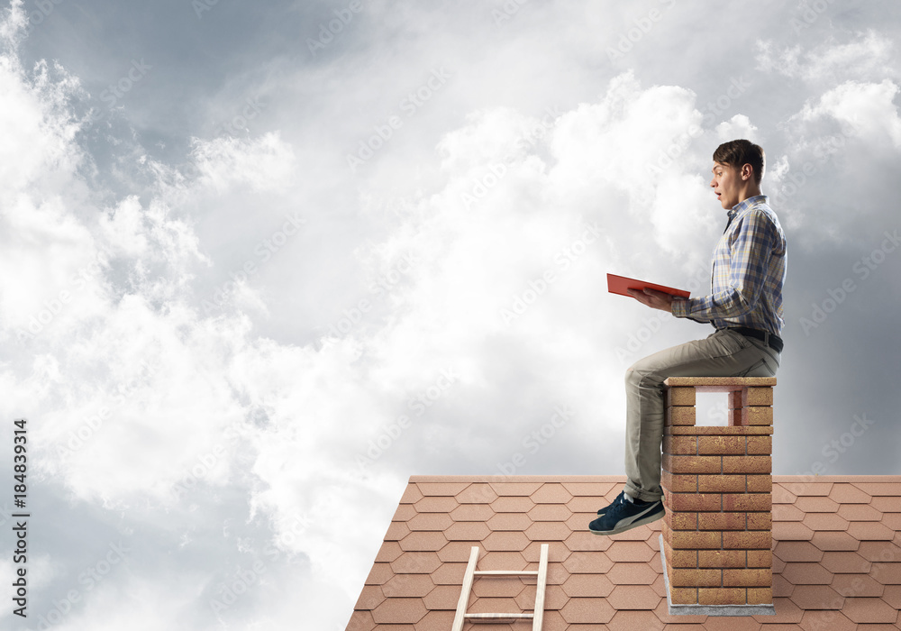 Handsome man on brick roof against cloud scape reading book Handsome man on brick roof against cloud scape reading book
