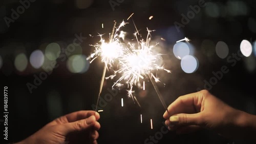 Hands of an unrecognizable man and woman holding sparklers. A blurred night background. Handheld real time establishing shot