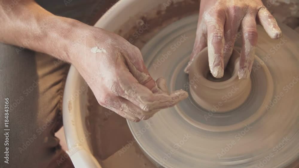 Rotating potter's wheel and clay ware on it (vase): taken from above. Hands in clay. Pottery: male ceramist creates a hand made clay product. Process of rotation of potter's wheel, hands of ceramist Rotating potter's wheel and clay ware on it (vase): taken from above. Hands in clay. Pottery: male ceramist creates a hand made clay product. Process of rotation of potter's wheel, hands of ceramist