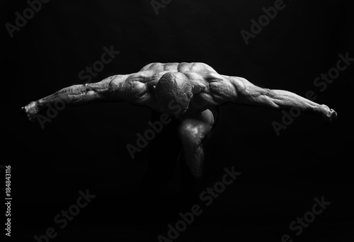 Muscular man with outstretched arms to the side and his head down on dark
