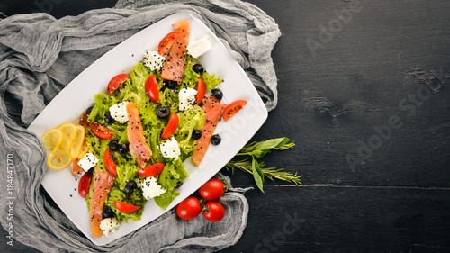 Salmon salad, feta cheese, salad leaves and fresh vegetables on the plate. On a wooden background. Top view. Free space for text.