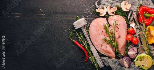 Raw chicken breast fillet with fresh vegetables and rosemary and spices on a black wooden background. Top view. Free space for text.