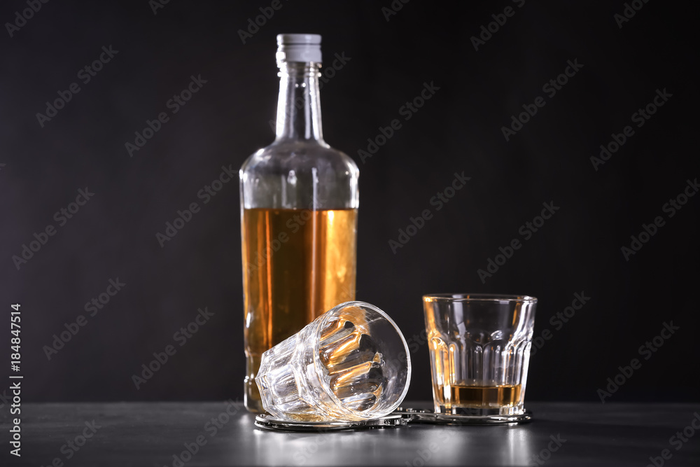 Bottle and glasses with handcuffs on dark background. Alcohol dependence concept Bottle and glasses with handcuffs on dark background. Alcohol dependence concept