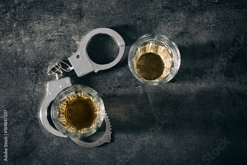 Glasses with handcuffs on grey background. Alcohol dependence concept