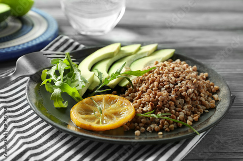 Plate with tasty buckwheat porridge and avocado on wooden table, closeup